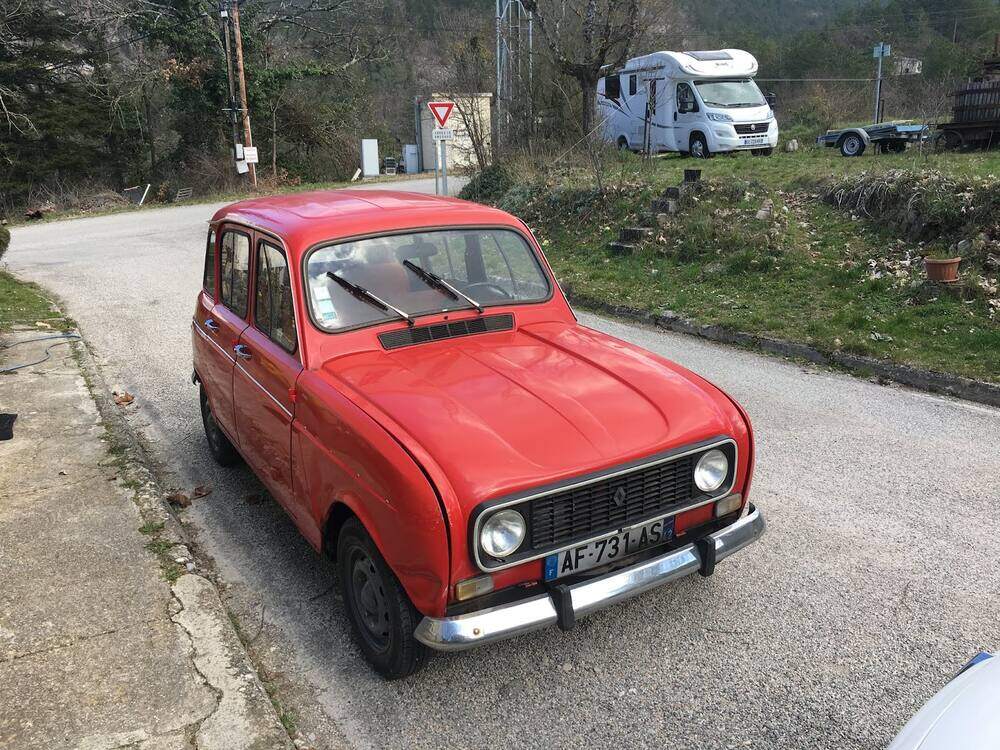 Renault 4 rouge garée au bord d'une petite route de campagne